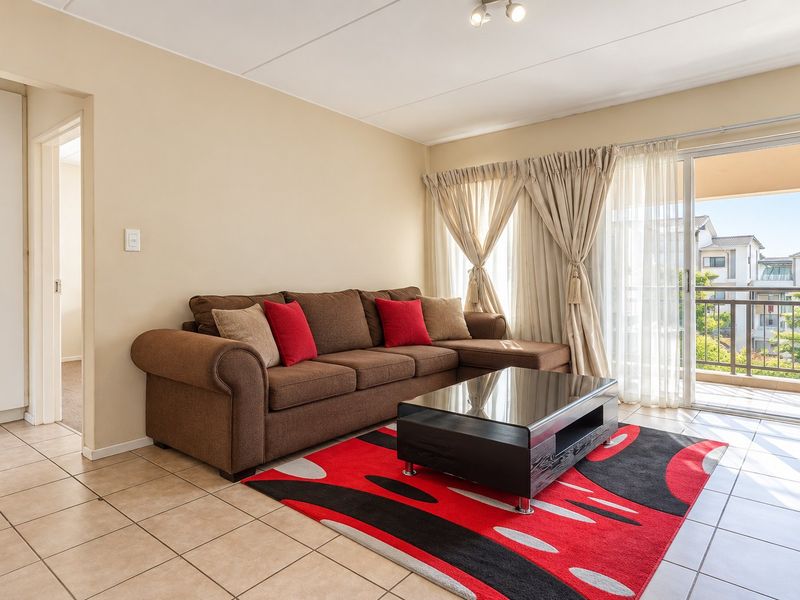 A bright living room featuring tiled flooring and a large sliding glass door providing access to an outdoor balcony area.