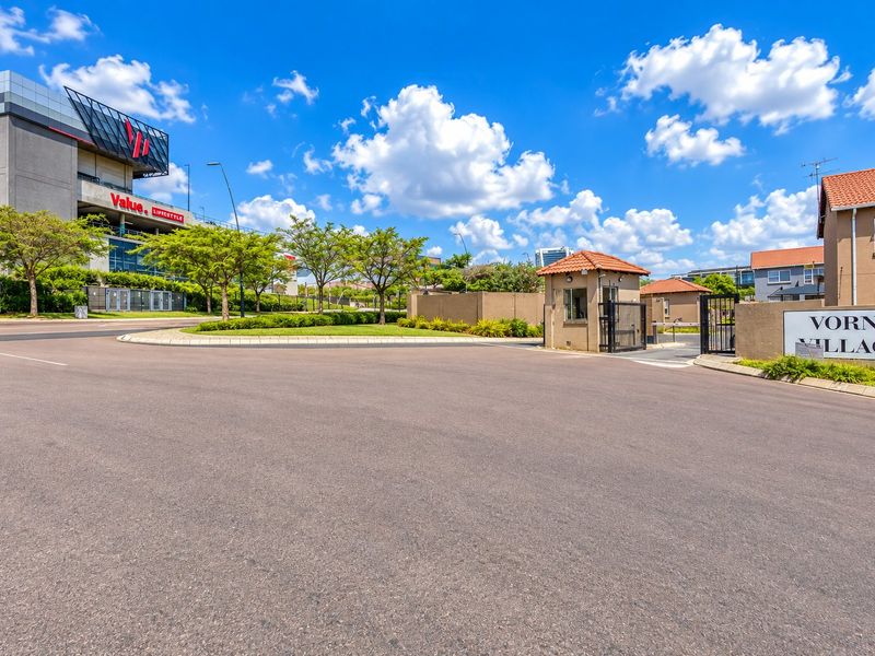 The entrance to Vorna Village featuring a secure gated access point, guard house, and paved driveway with clear signage.