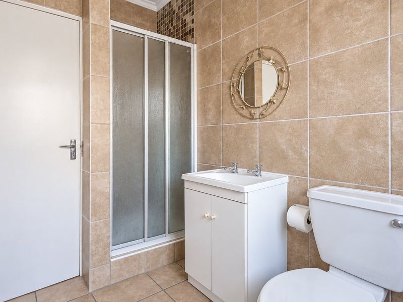 A functional bathroom featuring a shower enclosure, vanity cabinet with basin, and toilet, finished with neutral wall and floor tiling.