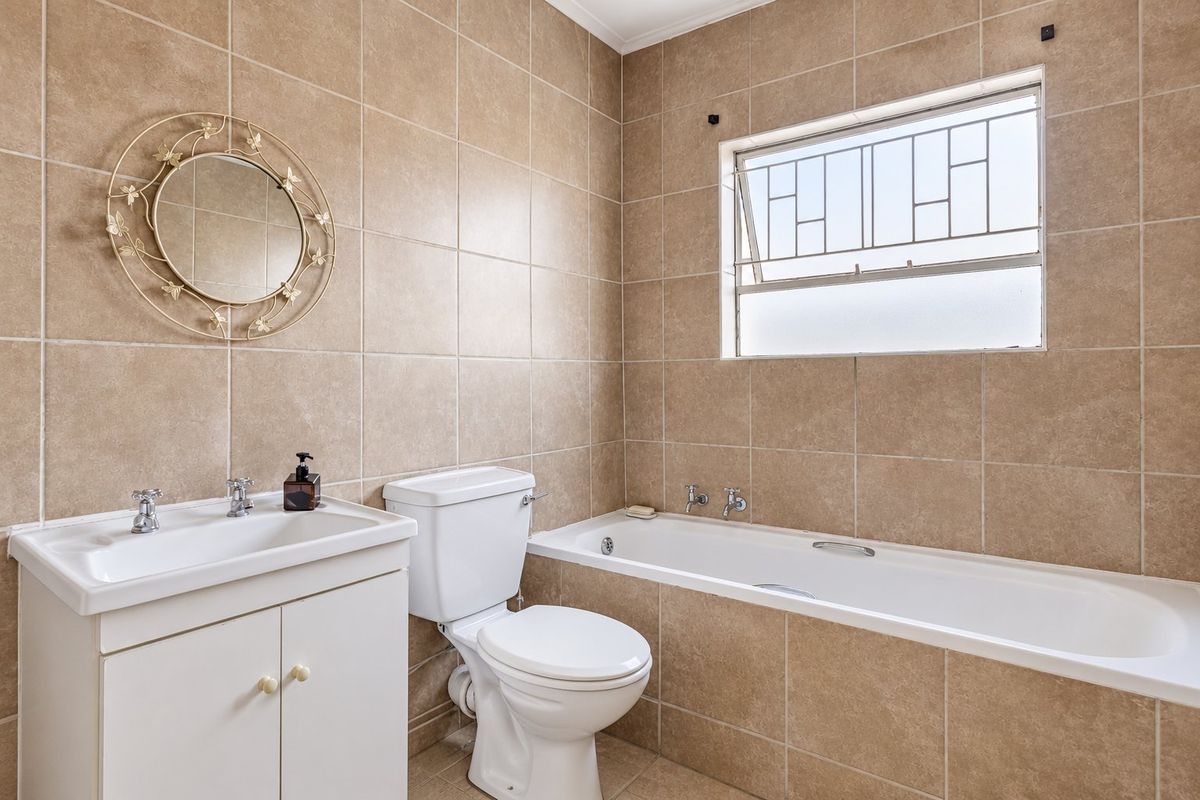 A functional bathroom featuring a vanity cabinet, toilet, and bathtub with neutral wall and floor tiling.