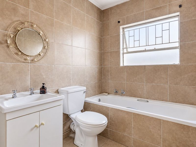 A functional bathroom featuring a vanity cabinet, toilet, and bathtub with neutral wall and floor tiling.