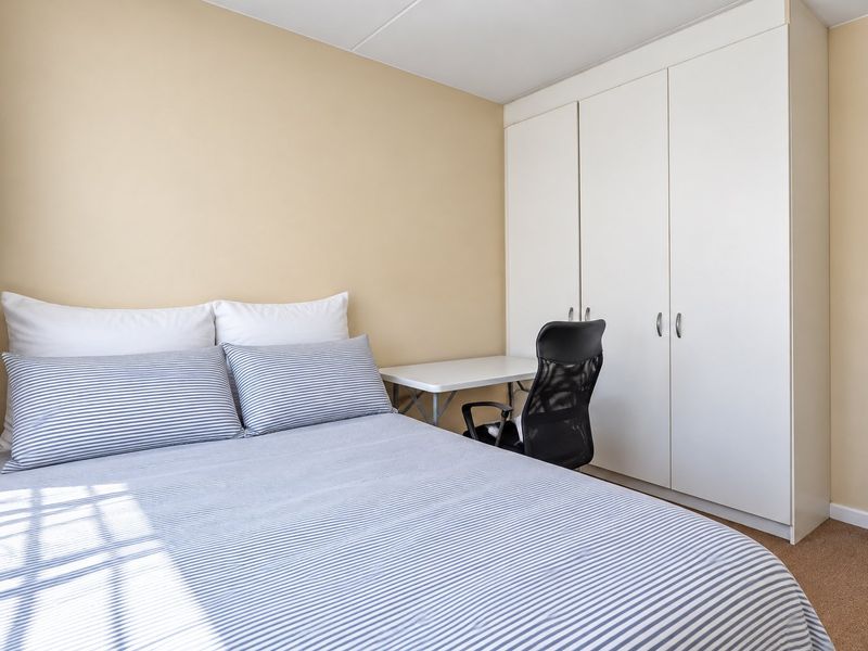 A functional bedroom featuring neutral wall tones, carpeted flooring, and a practical built-in wardrobe for storage.