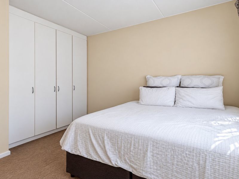 A well-maintained bedroom featuring neutral wall tones, carpeted flooring, and a spacious white built-in wardrobe for ample storage.