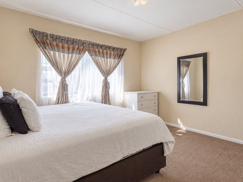 A well-lit bedroom featuring neutral wall tones, carpeted flooring, and a window with installed curtain tracks.
