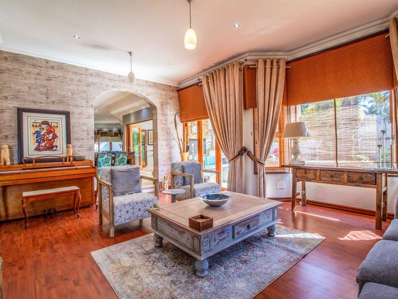 A bright and inviting living room featuring warm laminate flooring, a classic archway, and a large bay window that allows for ample natural light.