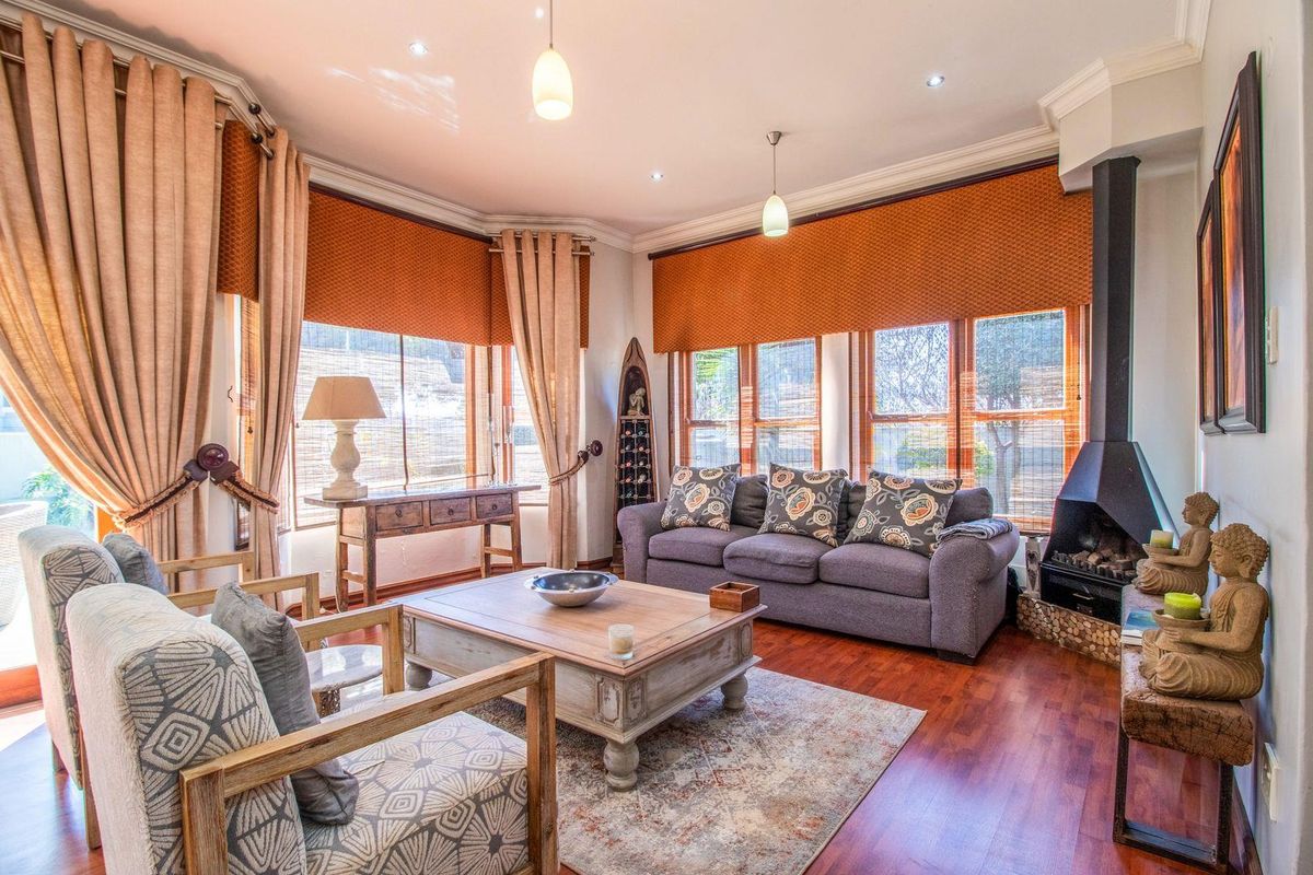 A well-lit living room featuring warm hardwood flooring, a modern freestanding fireplace, and large windows with custom window treatments.