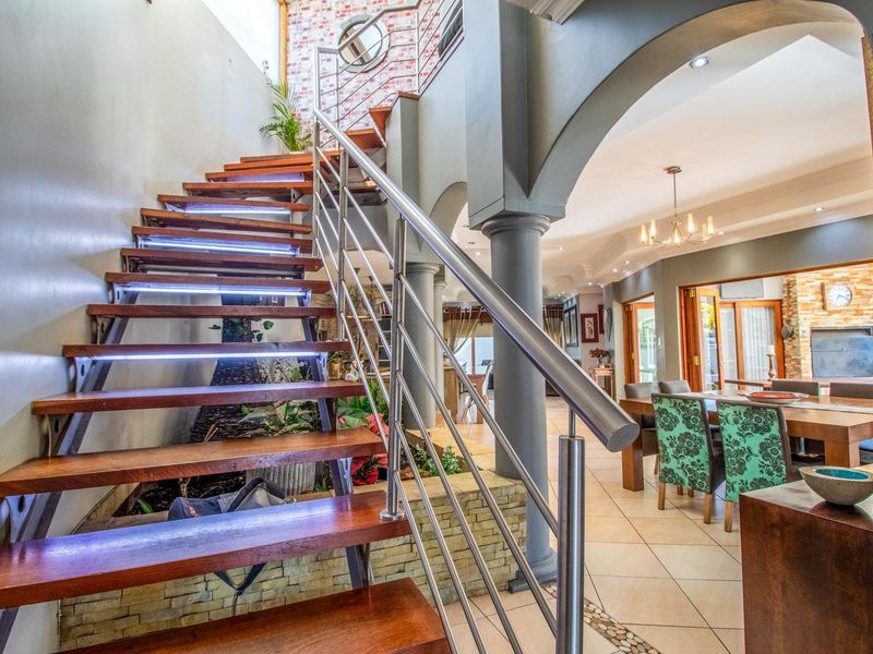 Grand entrance featuring a modern timber staircase with stainless steel balustrade, stone feature wall, and open-plan access to the dining and living areas.