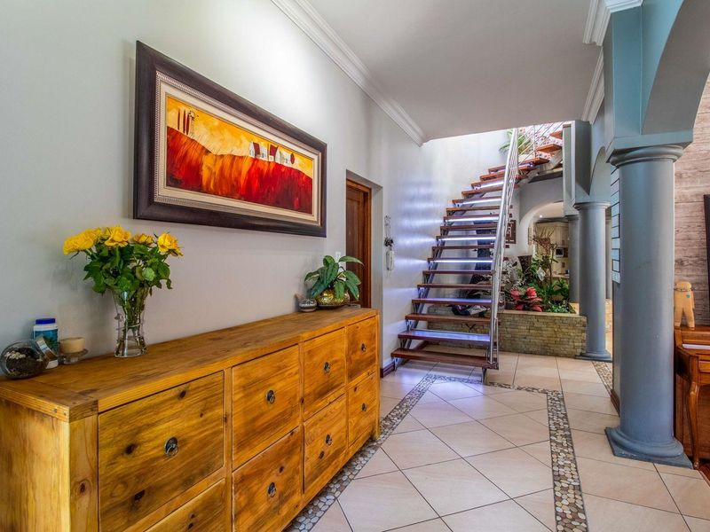 Spacious entrance hall featuring a modern open-tread staircase, decorative columns, and elegant tiled flooring with stone inlay detailing.