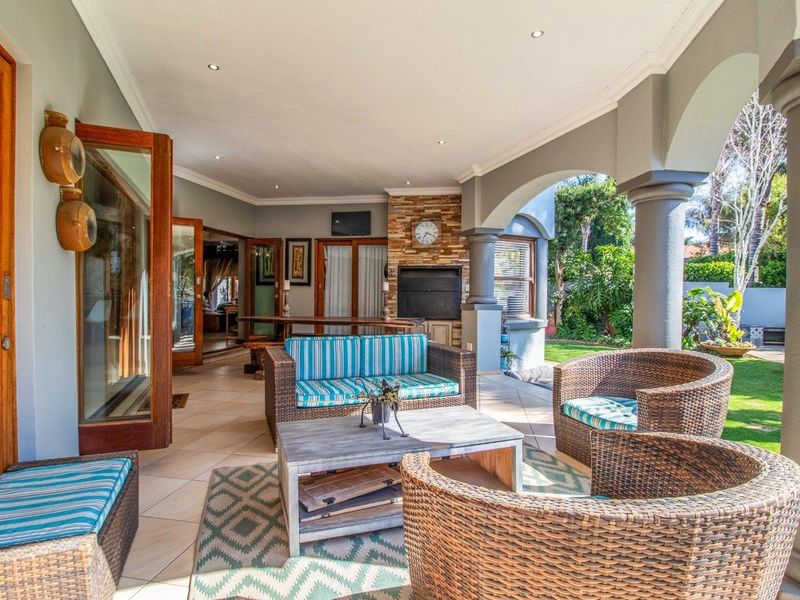 Spacious covered patio featuring a built-in fireplace with stone cladding, tiled flooring, and arched columns, providing seamless indoor-outdoor flow to the garden.