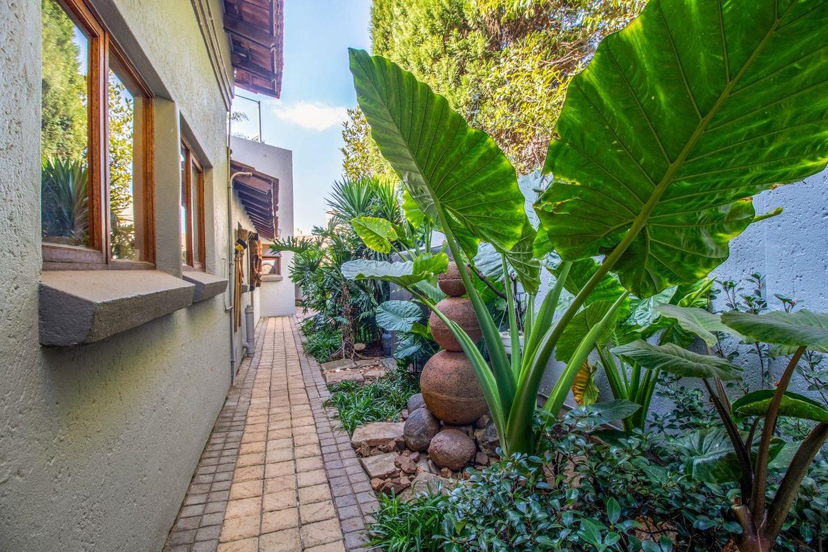 A well-maintained side garden path featuring stone paving, lush tropical landscaping, and a decorative stone water feature alongside the house exterior.