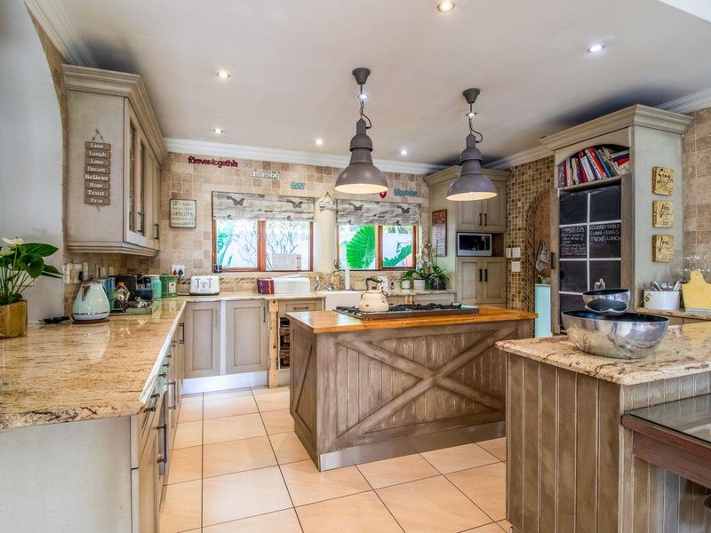 A well-appointed kitchen featuring granite countertops, a central island with a gas hob, farmhouse sink, and ample built-in cabinetry with warm, rustic finishes.