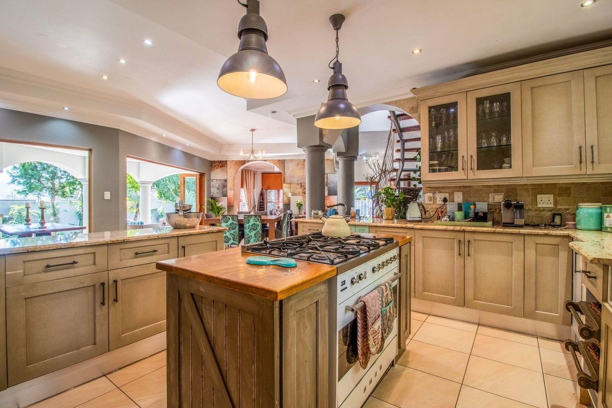 Spacious kitchen featuring a central island with a gas stove, granite countertops, custom cabinetry, and elegant pendant lighting, seamlessly flowing into the living area.