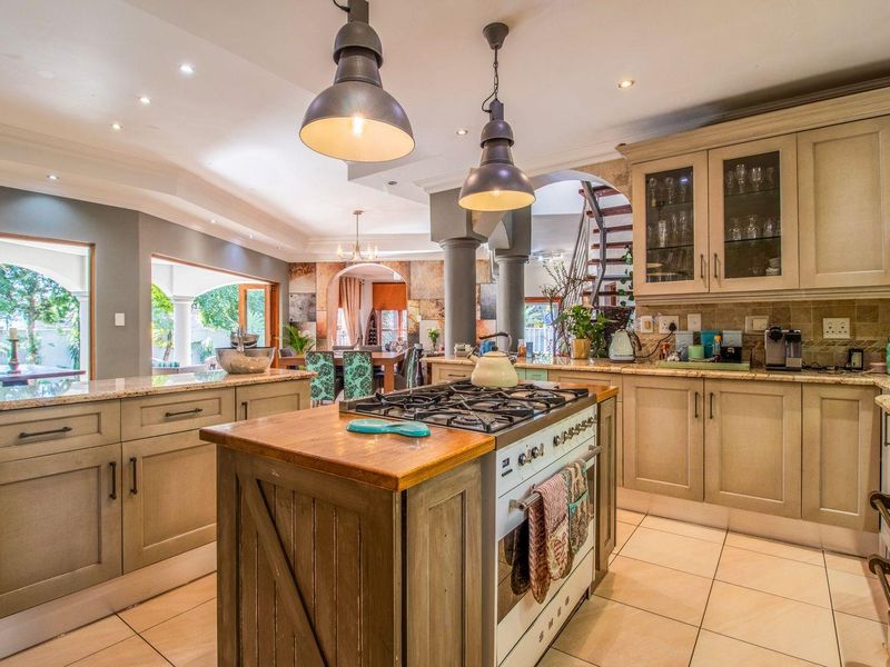 Spacious kitchen featuring a central island with a gas stove, granite countertops, custom cabinetry, and elegant pendant lighting, seamlessly flowing into the living area.