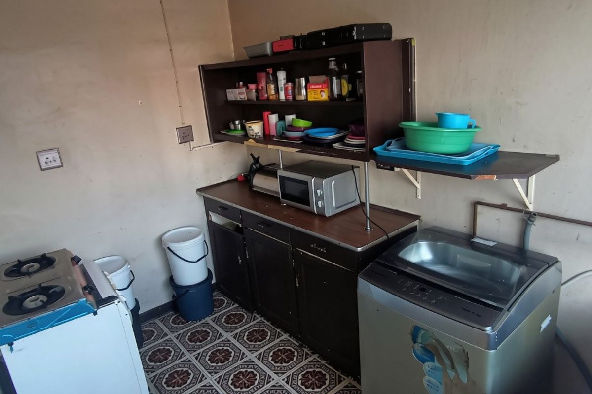 A functional scullery or utility area featuring built-in cabinetry, wall-mounted shelving, and plumbing connections for laundry or wash-up tasks.