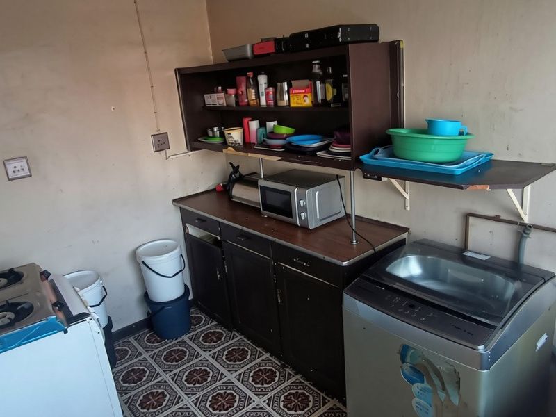 A functional scullery or utility area featuring built-in cabinetry, wall-mounted shelving, and plumbing connections for laundry or wash-up tasks.