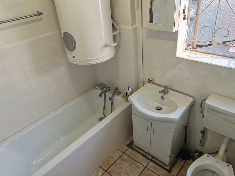A compact bathroom featuring a bathtub, wall-mounted water heater, vanity basin, and toilet, with tiled finishes throughout.