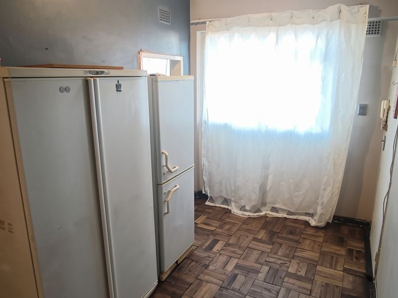 A functional laundry or utility space featuring classic parquet flooring and a window with curtain covering.