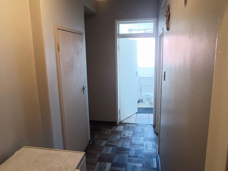 A narrow hallway featuring parquet flooring and access to an adjacent bathroom, showing signs of wear and requiring cosmetic updates.
