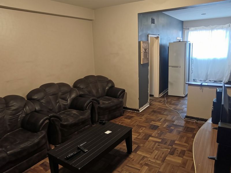 Open plan living area featuring traditional parquet flooring and a breakfast bar, offering a functional layout with potential for cosmetic updates.