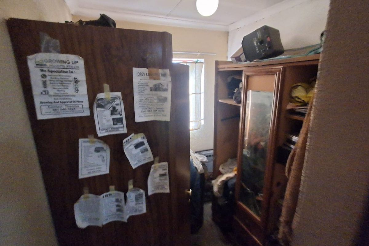 A small bedroom space featuring a built-in cupboard, currently cluttered and in need of cosmetic updates and maintenance.