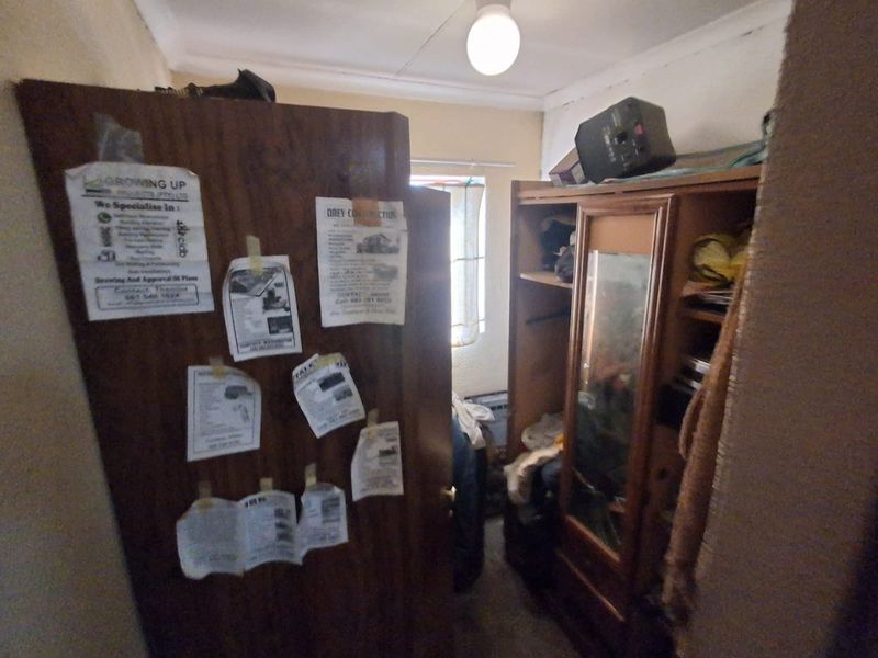 A small bedroom space featuring a built-in cupboard, currently cluttered and in need of cosmetic updates and maintenance.