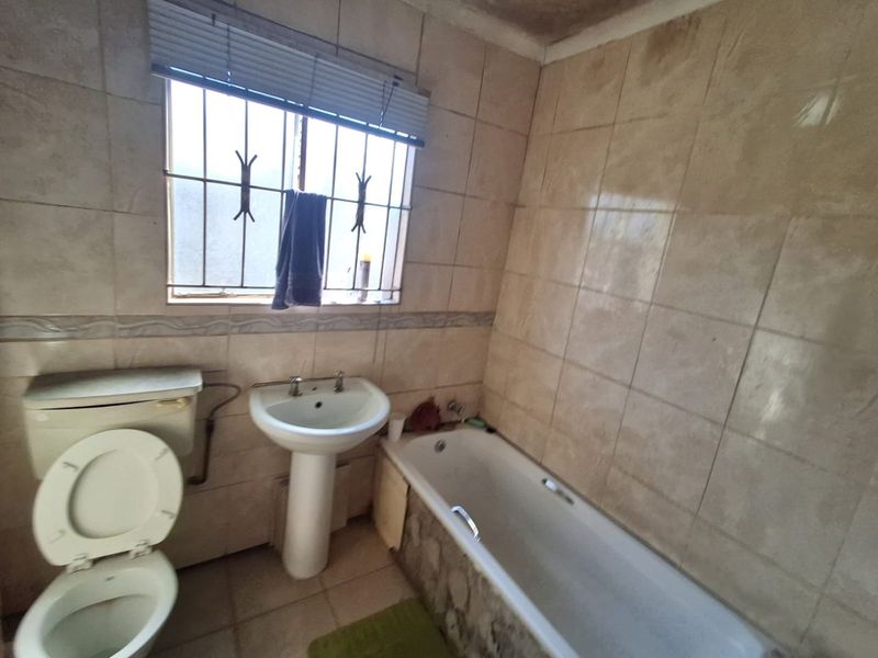 A dated bathroom featuring a pedestal basin, bathtub, and toilet with tiled walls and floor, requiring cosmetic updates and maintenance.