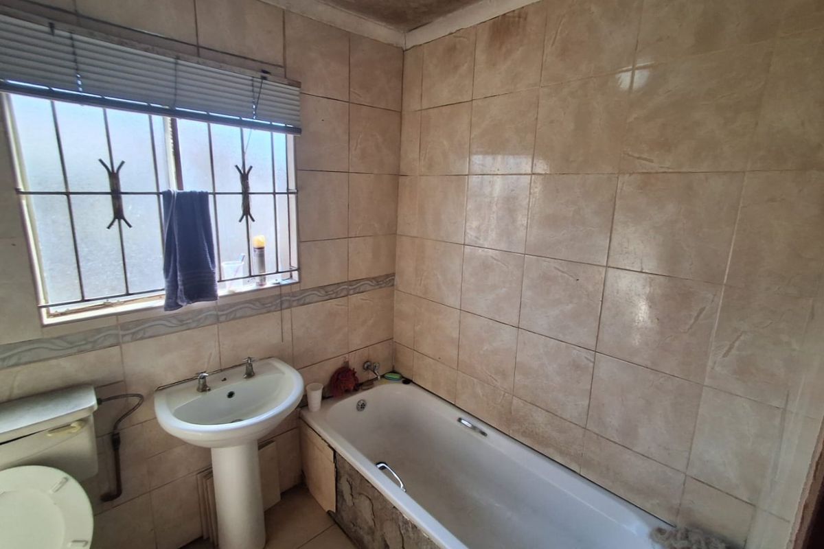 A dated bathroom featuring a pedestal basin, bathtub, and tiled finishes, requiring renovation to address ceiling staining and general wear.