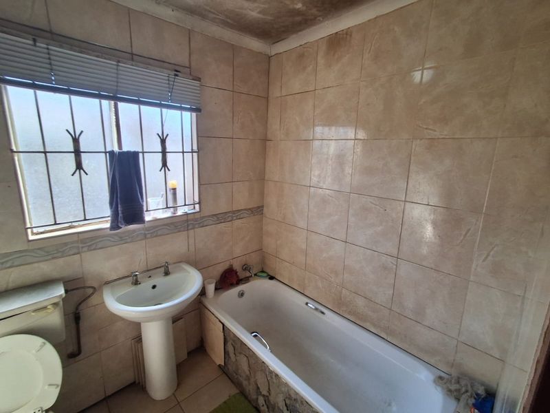 A dated bathroom featuring a pedestal basin, bathtub, and tiled finishes, requiring renovation to address ceiling staining and general wear.