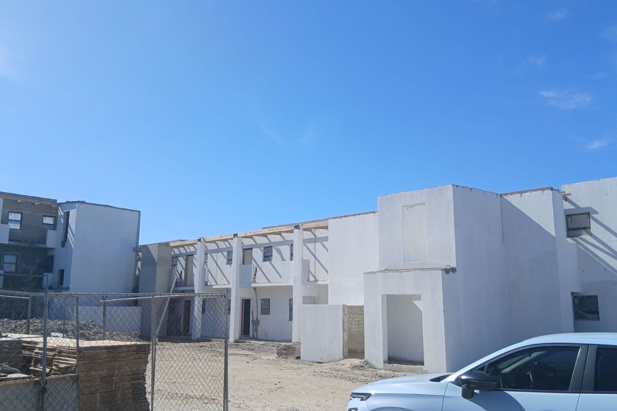 Exterior view of an apartment complex currently under construction, featuring unfinished concrete walls and exposed timber roof framing.