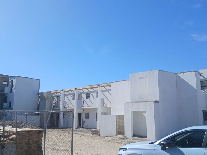 Exterior view of an apartment complex currently under construction, featuring unfinished concrete walls and exposed timber roof framing.