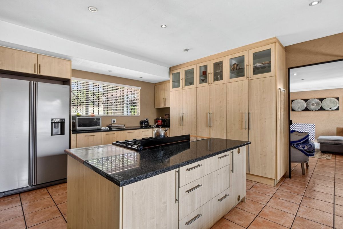 A functional kitchen featuring light wood cabinetry, a central island with a granite countertop, gas cooktop, and tiled flooring.