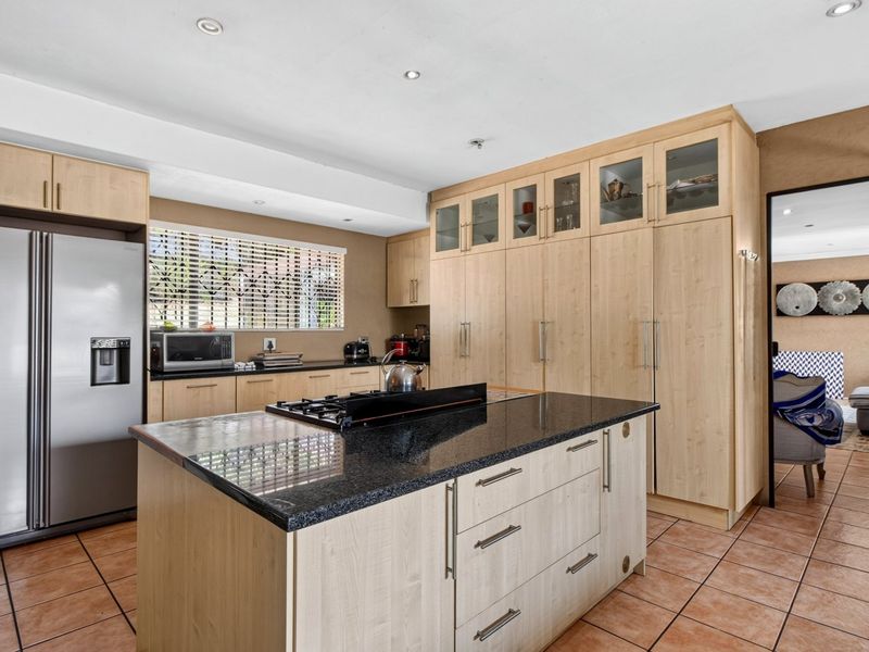 A functional kitchen featuring light wood cabinetry, a central island with a granite countertop, gas cooktop, and tiled flooring.