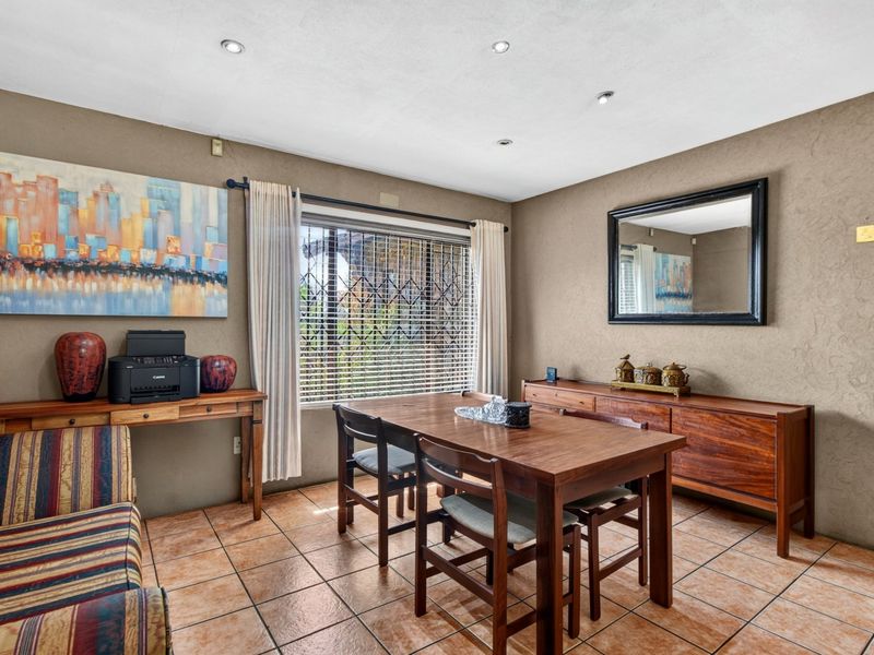 A dining room featuring ceramic floor tiles, recessed downlighting, and a window fitted with a security gate and blinds.