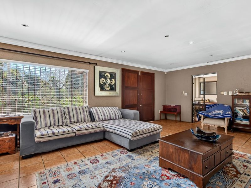 Spacious living room featuring tiled flooring, recessed downlighting, and large windows with security bars, providing access to adjacent areas through double wooden doors.