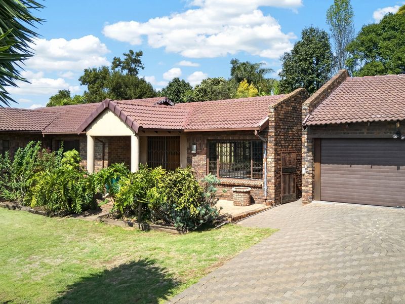 A well-maintained face brick house featuring a tiled roof, paved driveway, and an integrated garage, set within a landscaped garden.