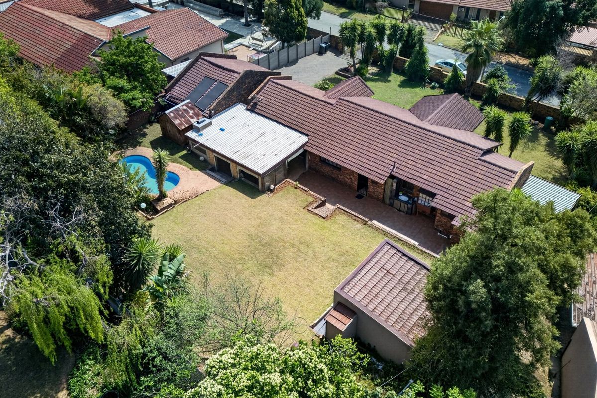 Aerial view of a residential property featuring a tiled roof, swimming pool, spacious garden, and a covered patio area.