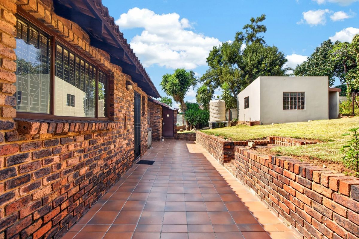Rear exterior view featuring a tiled patio, face brick facade, retaining walls, and a separate outbuilding set within a garden area.