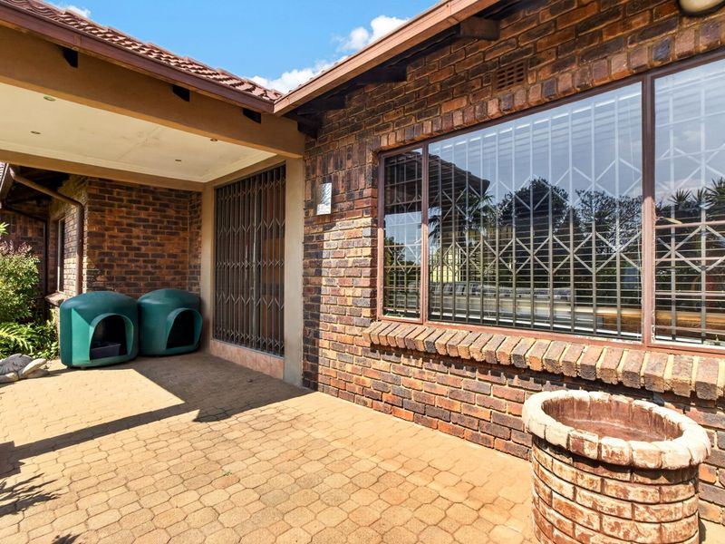 A covered brick-paved patio area featuring face brick walls, recessed lighting, and secure metal security gates over the windows and doors.