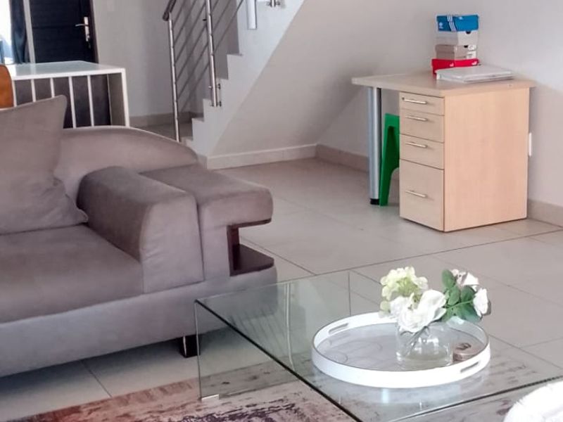 A bright living room featuring tiled flooring and a modern staircase with a stainless steel balustrade.