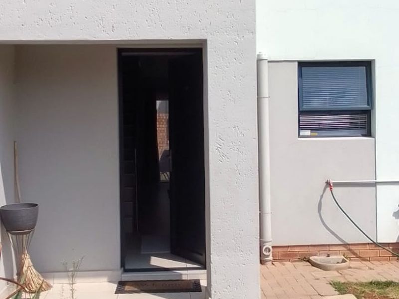 Front entrance of a modern two-story house featuring a paved walkway, tiled porch area, and contemporary aluminium window frames.
