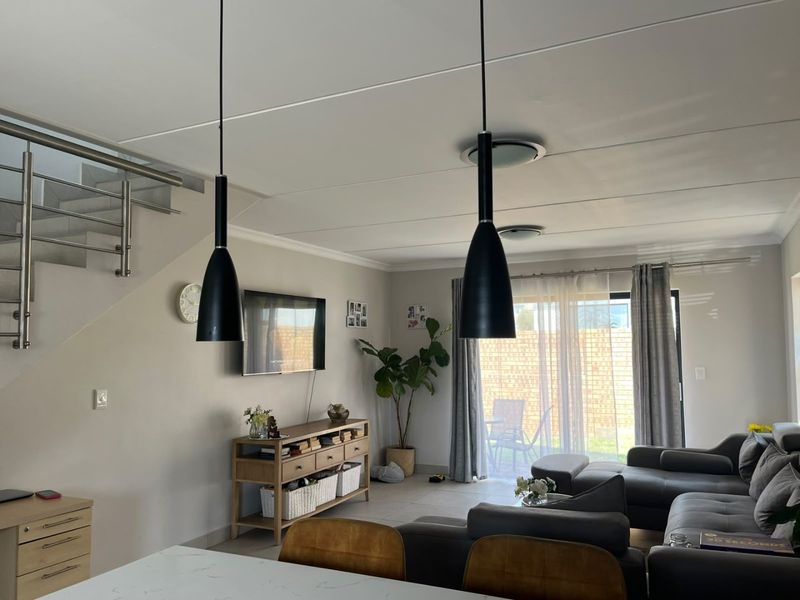 Open plan living area featuring tiled floors, modern pendant lighting, and a staircase with a stainless steel balustrade, leading to a rear patio.