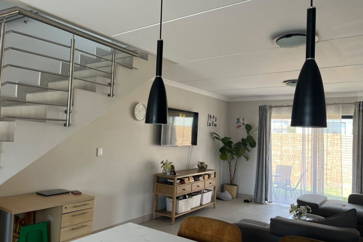 Open-plan living area featuring a modern staircase with stainless steel balustrades, tiled flooring, and direct access to the outdoor patio through sliding glass doors.