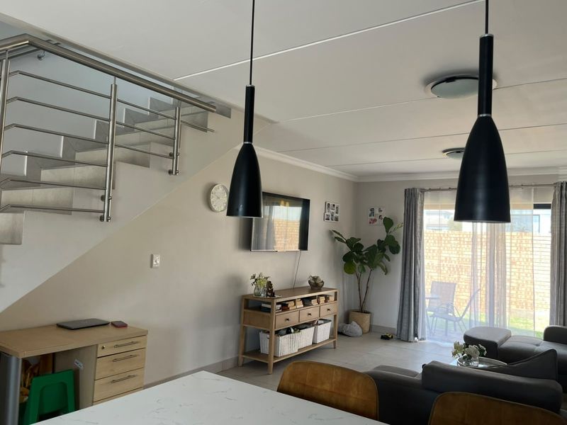 Open-plan living area featuring a modern staircase with stainless steel balustrades, tiled flooring, and direct access to the outdoor patio through sliding glass doors.
