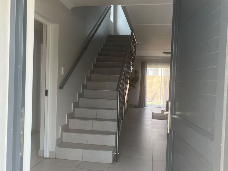 Bright entrance hall featuring a modern tiled staircase with a stainless steel balustrade, leading into an open-plan living area with access to the rear patio.