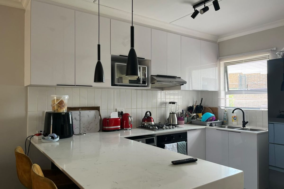 Modern kitchen featuring white cabinetry, quartz countertops, a gas hob, and a subway tile backsplash with integrated appliances and contemporary lighting.