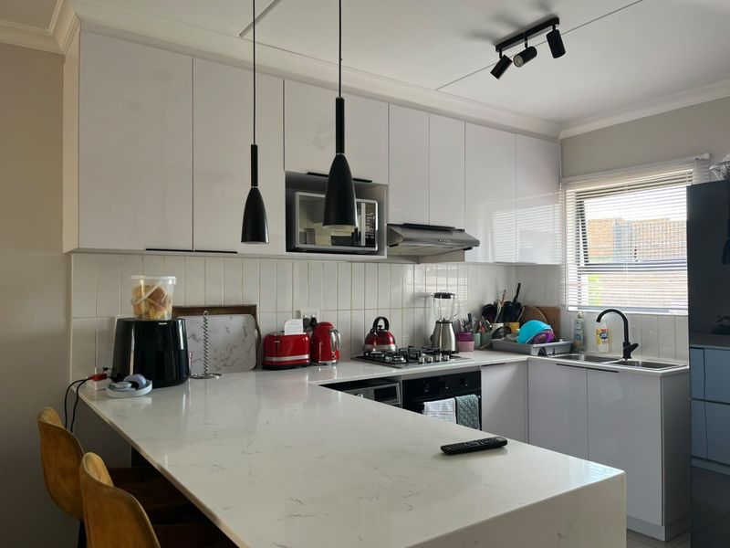 Modern kitchen featuring white cabinetry, quartz countertops, a gas hob, and a subway tile backsplash with integrated appliances and contemporary lighting.