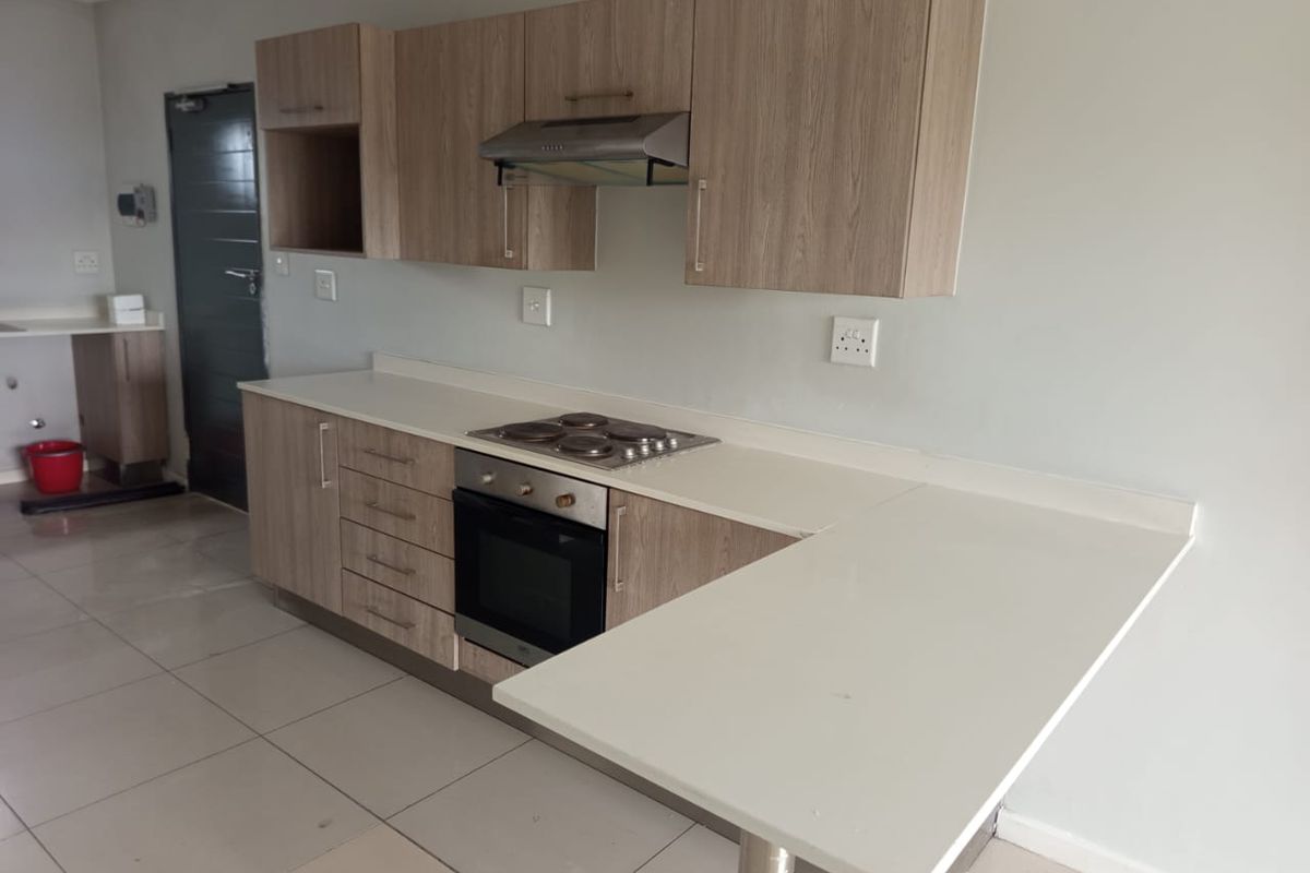 Modern kitchen featuring light wood-finish cabinetry, stone countertops, a breakfast bar, and integrated appliances including an oven and hob.