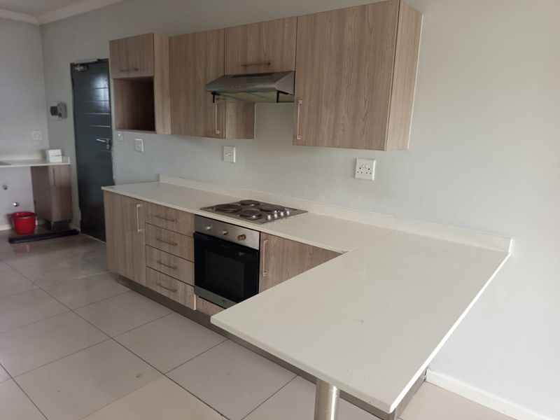 Modern kitchen featuring light wood-finish cabinetry, stone countertops, a breakfast bar, and integrated appliances including an oven and hob.