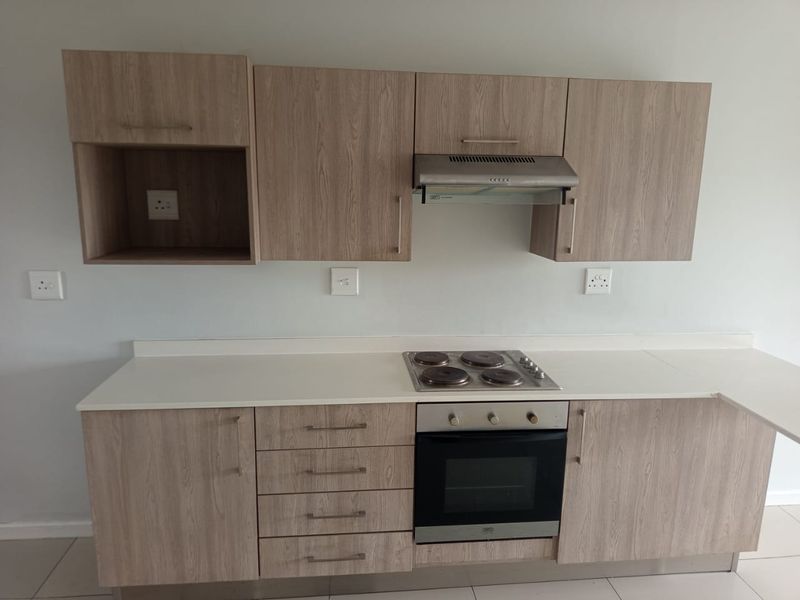 A clean, modern kitchen featuring light wood-grain cabinetry, white countertops, and integrated appliances including an electric hob, oven, and extractor fan.