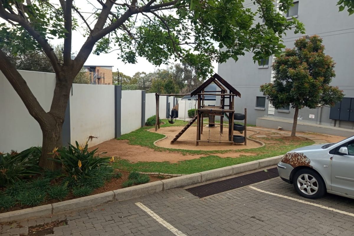 Communal outdoor area featuring a playground, paved parking bays, and perimeter walling within the apartment complex grounds.